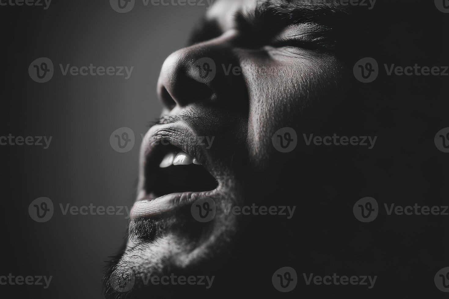 Man with dark hair screams in the darkness with open mouth photo
