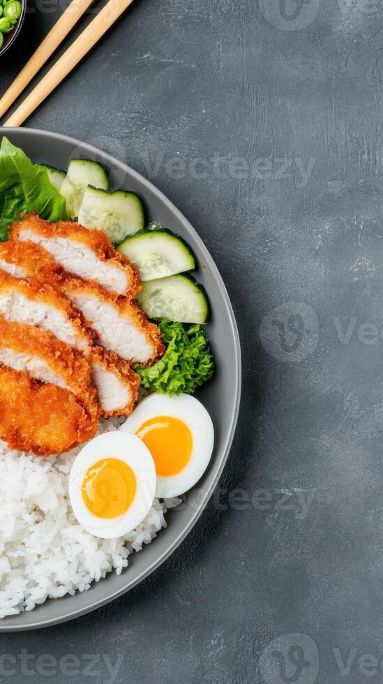 Chicken katsu over rice with vegetables, boiled egg, and chopsticks on a gray background photo