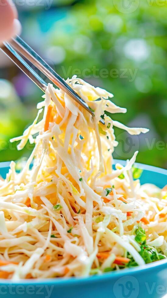 Chopsticks lift coleslaw in bowl outdoors. A fresh, colorful salad for lunch or picnic photo