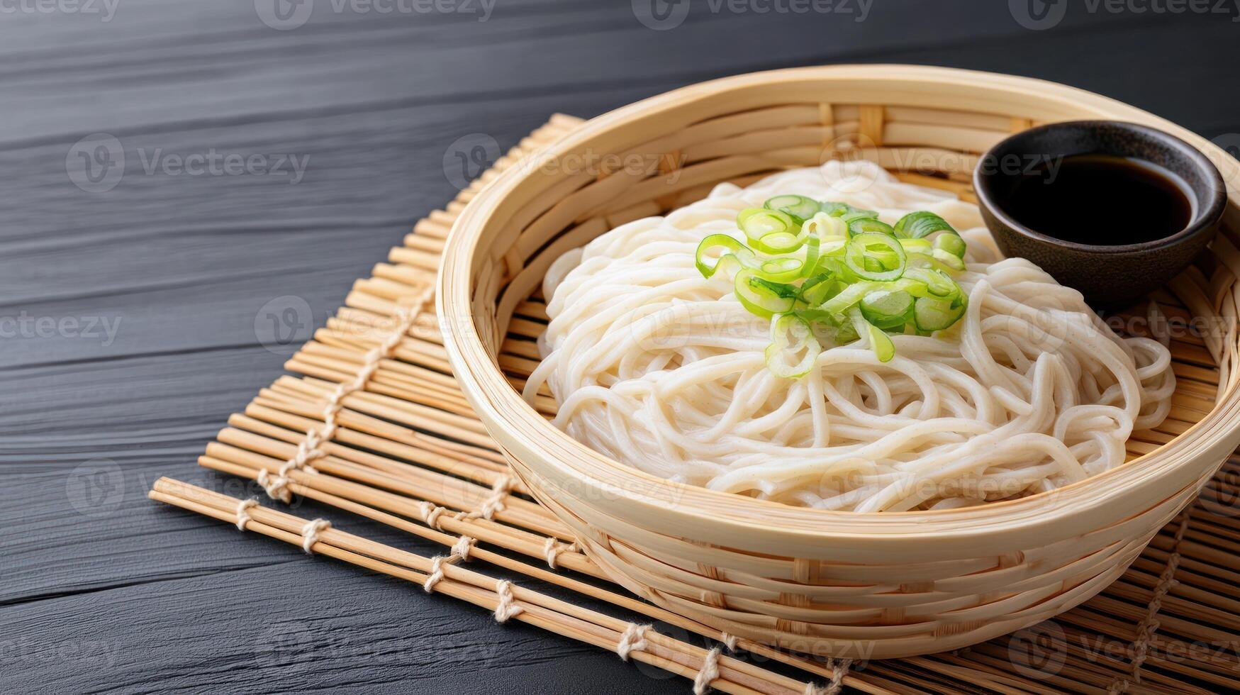 Noodles in a bamboo basket, topped with green onions and sauce, on a black wood table photo