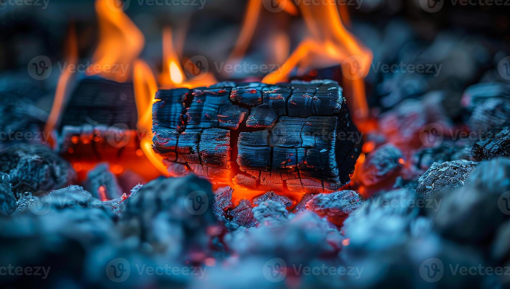 Dancing flames on glowing coals. Flickering flames illuminate charred logs resting on smoldering coals during a nighttime gathering. photo
