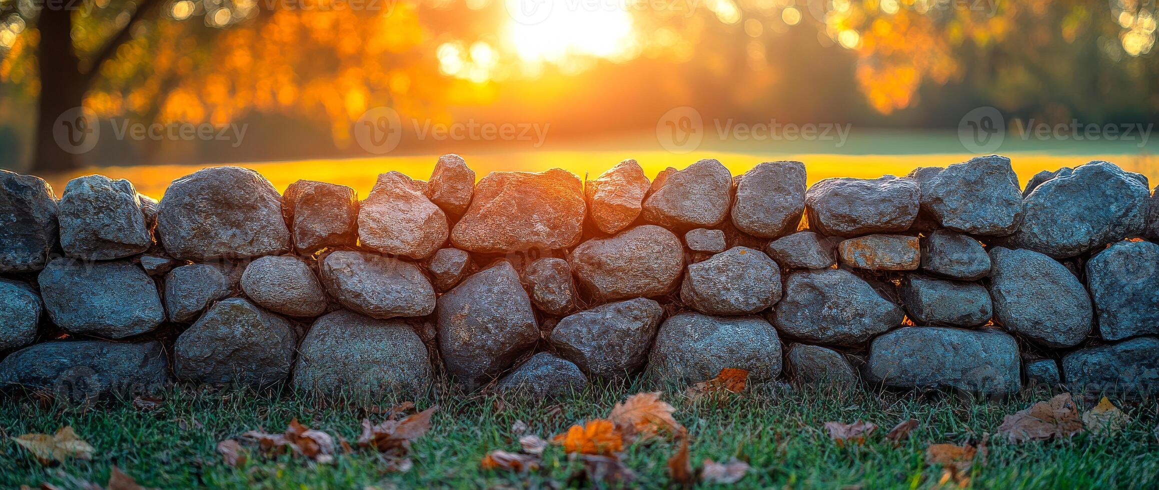 Sunset over stone wall in autumn park. A serene stone wall captures the warm glow of sunset, surrounded by fallen leaves in a tranquil park setting. photo