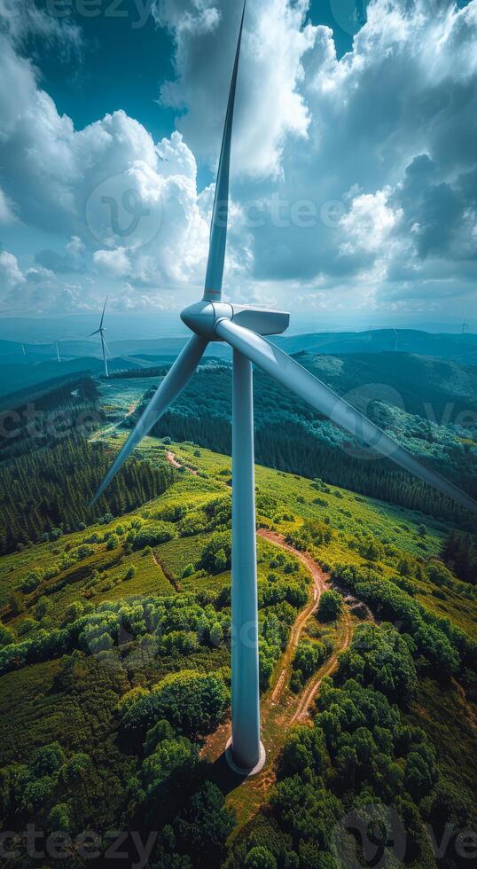 Turbine above green landscape. A towering wind turbine stands against a backdrop of rolling hills and green fields under a partly cloudy sky. photo
