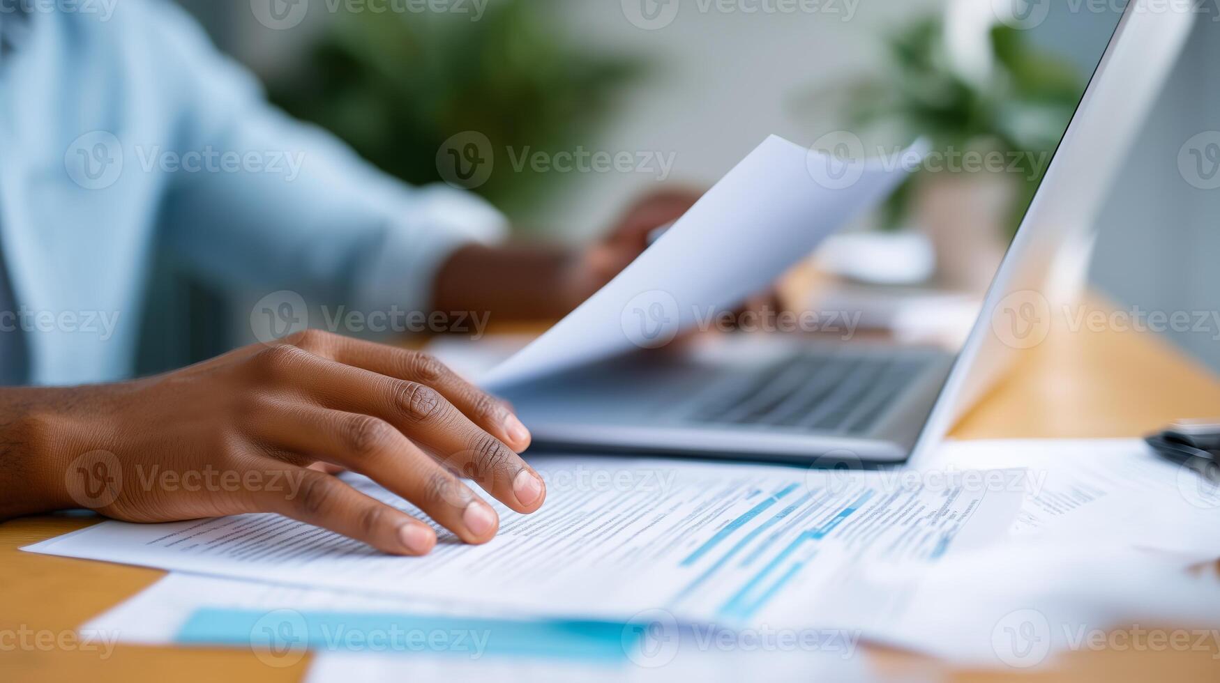 Focused individual working on documents while using a laptop in a well-lit office environment photo