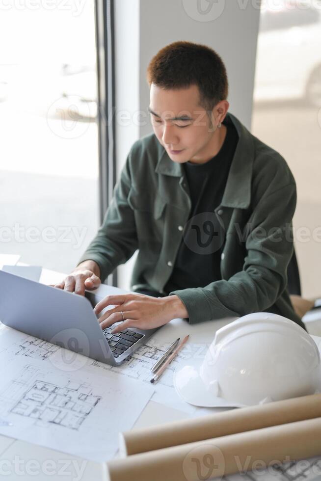 a man in a green jacket sitting at a table with a laptop photo