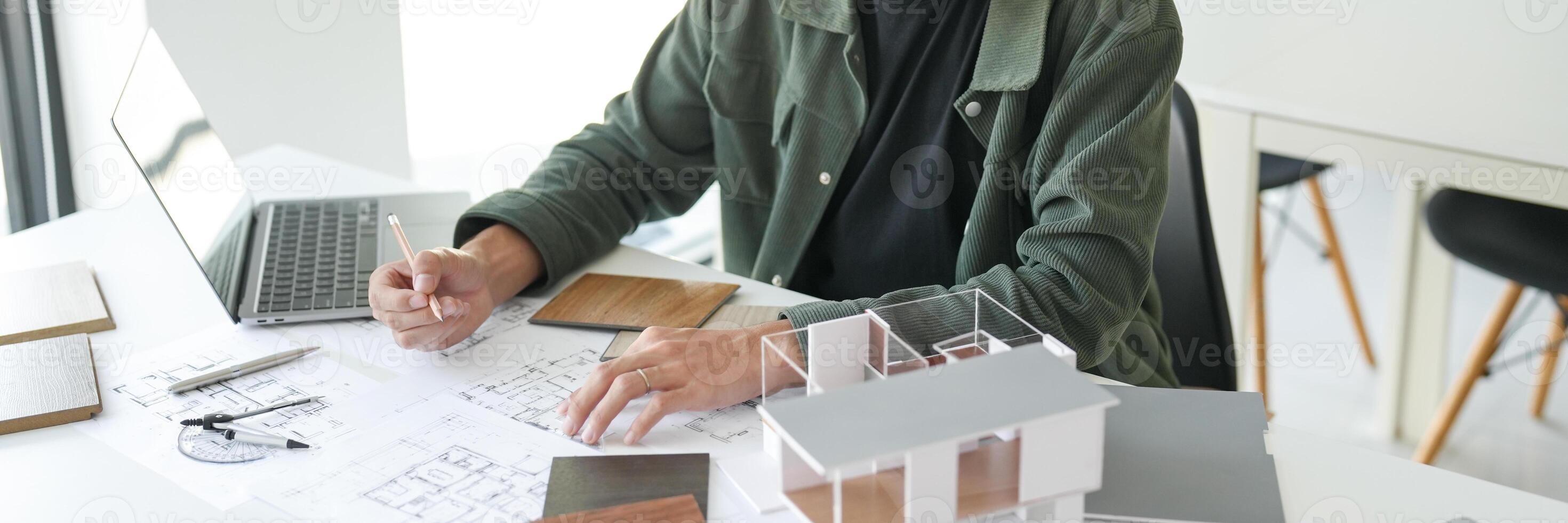 a man sitting at a table with a laptop and a model house photo