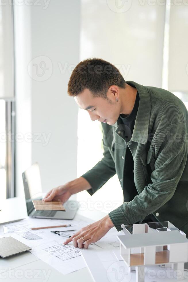 a man working on a laptop and looking at a blueprint photo