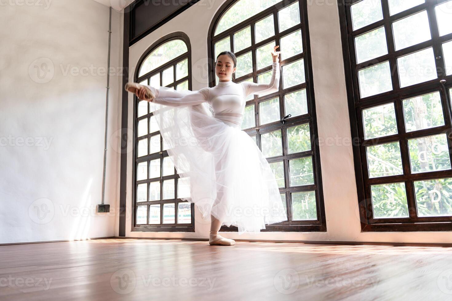 a woman in a white dress is dancing in front of large windows photo