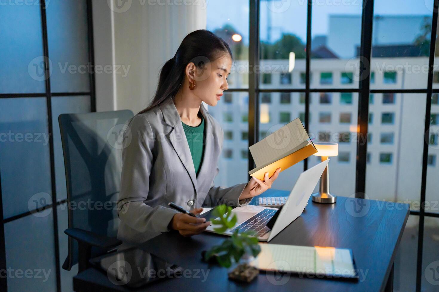 a woman in a business suit is sitting at a desk with a laptop at night photo