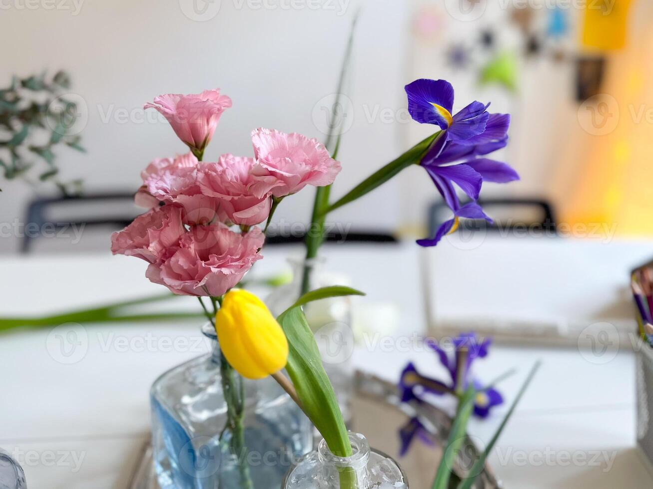 Pink flower in glass vase with blurred tulips and vases in background. Elegance, freshness, and home floral decor in spring. photo