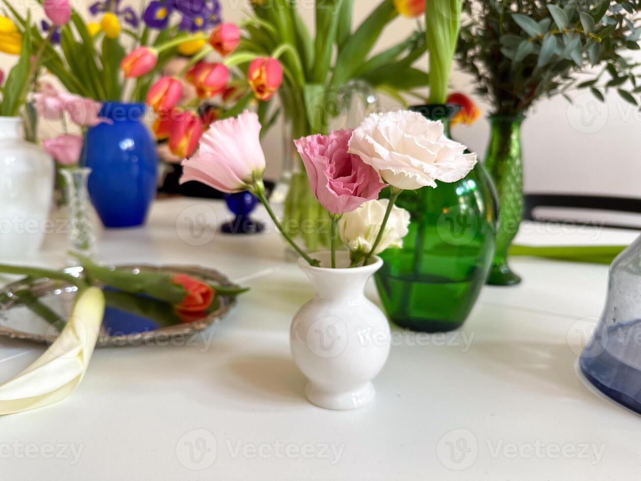 Pink and white lisianthus flowers in small white vase among colorful tulip arrangements. Home decoration and floral composition photo