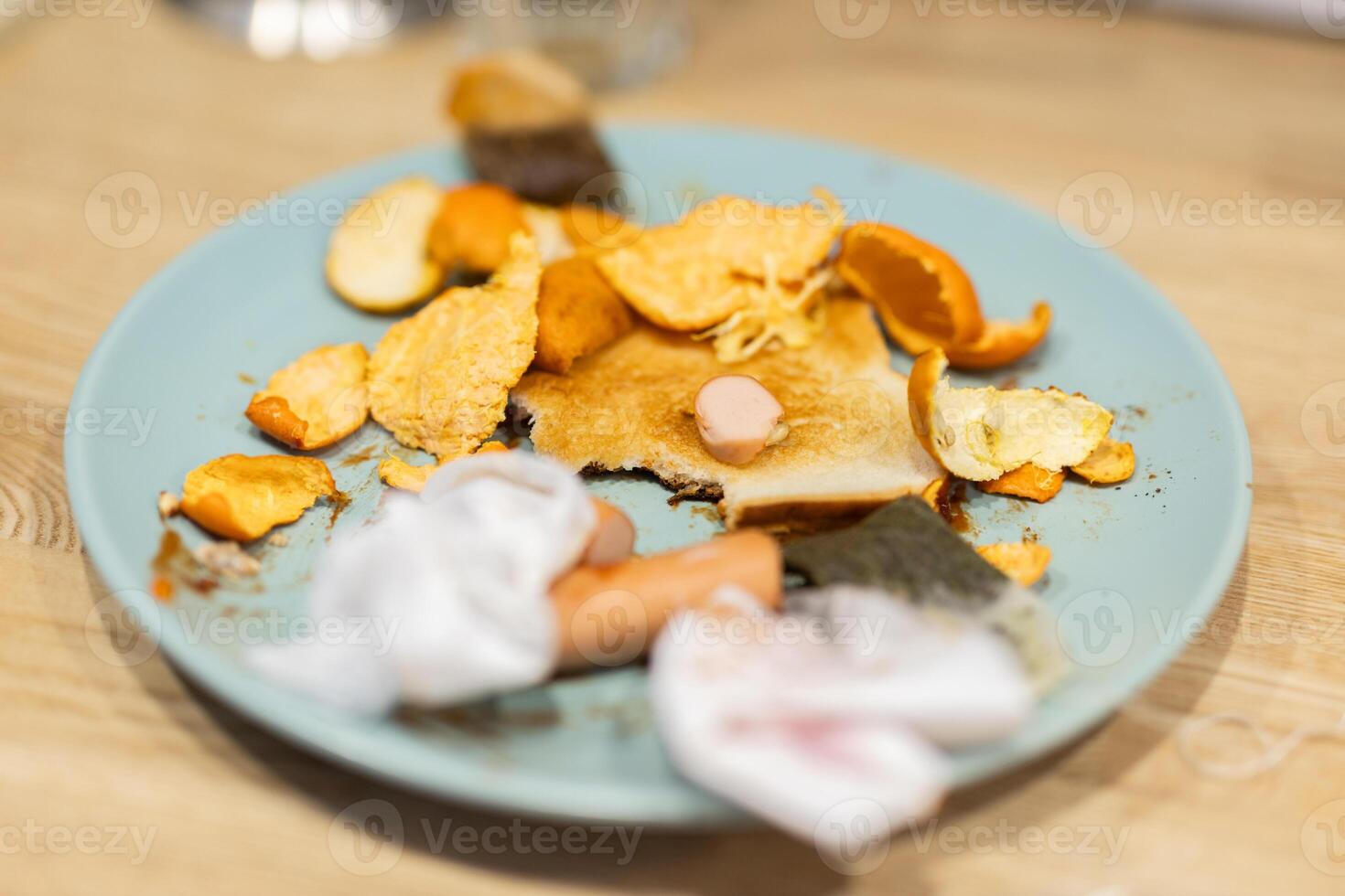 Dirty plate with food leftovers and trash on a kitchen table. Home neglect and everyday domestic mess in a cluttered environment. photo