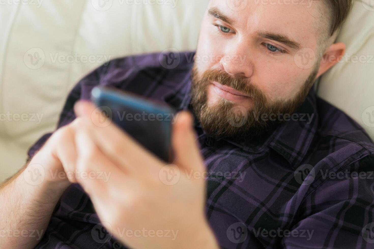 Bored lazy man close up relaxed and use smartphone for killing time alone in apartment - social media and gadget addiction concept photo
