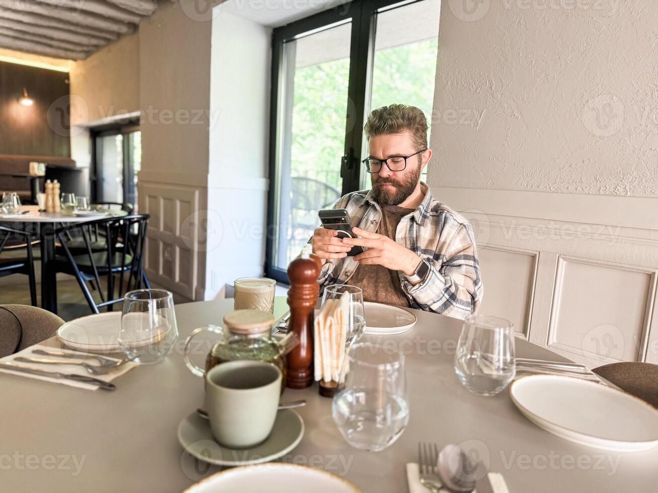 Handsome man browses his smartphone while waiting for coffee. Digital routine and urban cafe culture photo