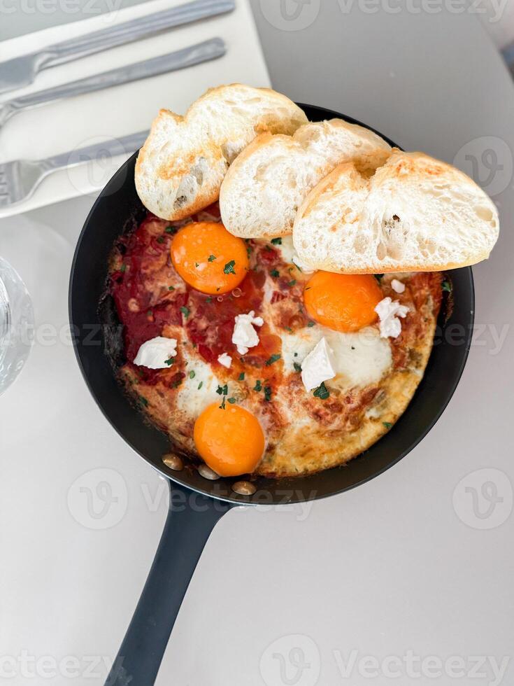 Shakshuka served hot in pan with bread slices. Top view photo