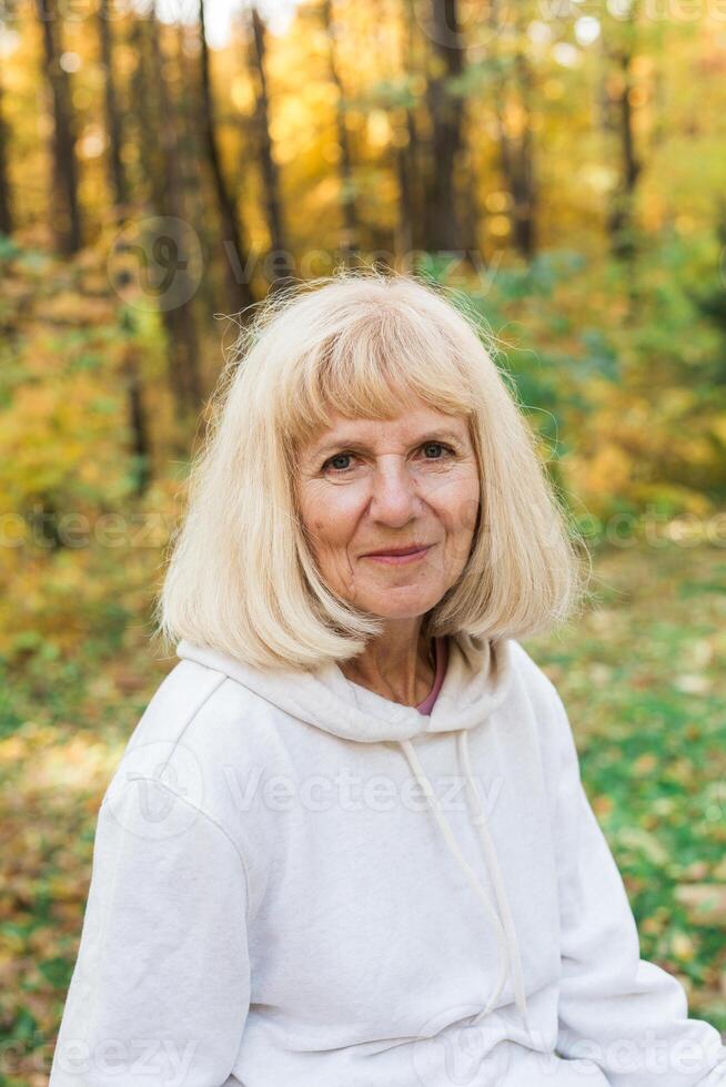 Mature woman portrait in autumn forest and smiling peacefully. Emotional well-being and connection with nature photo