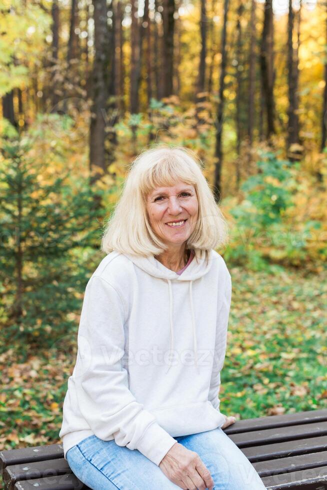 Senior woman relaxing on a bench in an autumn park. Concept of aging gracefully, wellbeing, emotional calmness, leisure and joy of simple outdoor pleasures photo