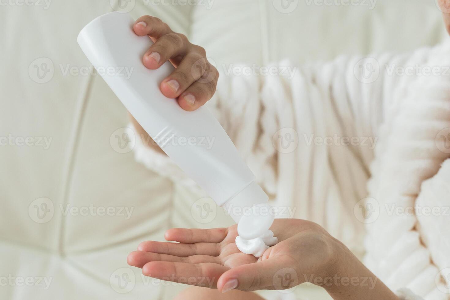 Applying lotion from white bottle at home. Concept of moisturizing, skincare treatment, beauty care. photo