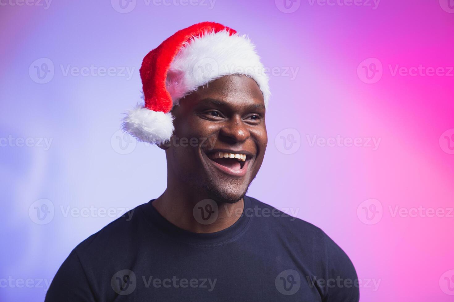 Portrait of positive handsome man in santa hat and casual t-shirt on colourful background, christmas time. Winter holidays and emotional people concept. photo