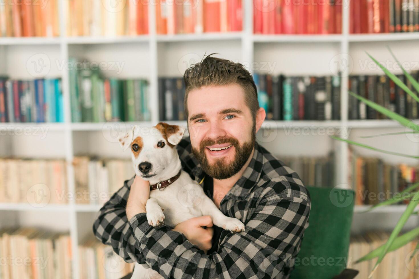 Male owner of jack russell terrier dog, feels responsibility of caring about pet, standing against bookshelves background photo
