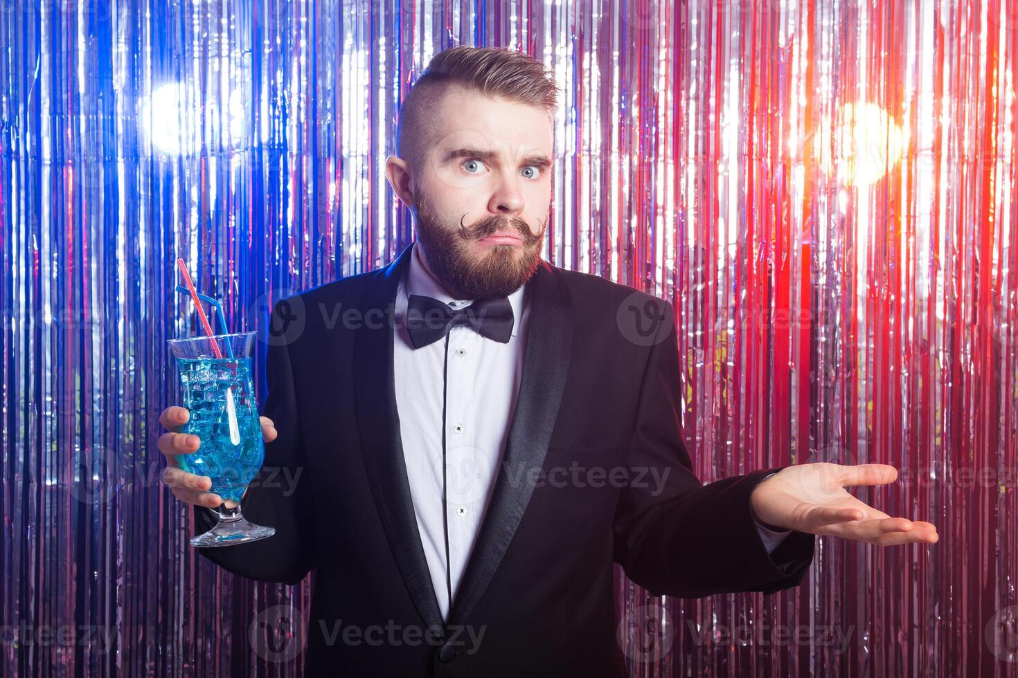 Club party, emotion and holidays concept - Portrait of elegant surprised handsome man in a expensive suit holds blue cocktail on shiny background. photo