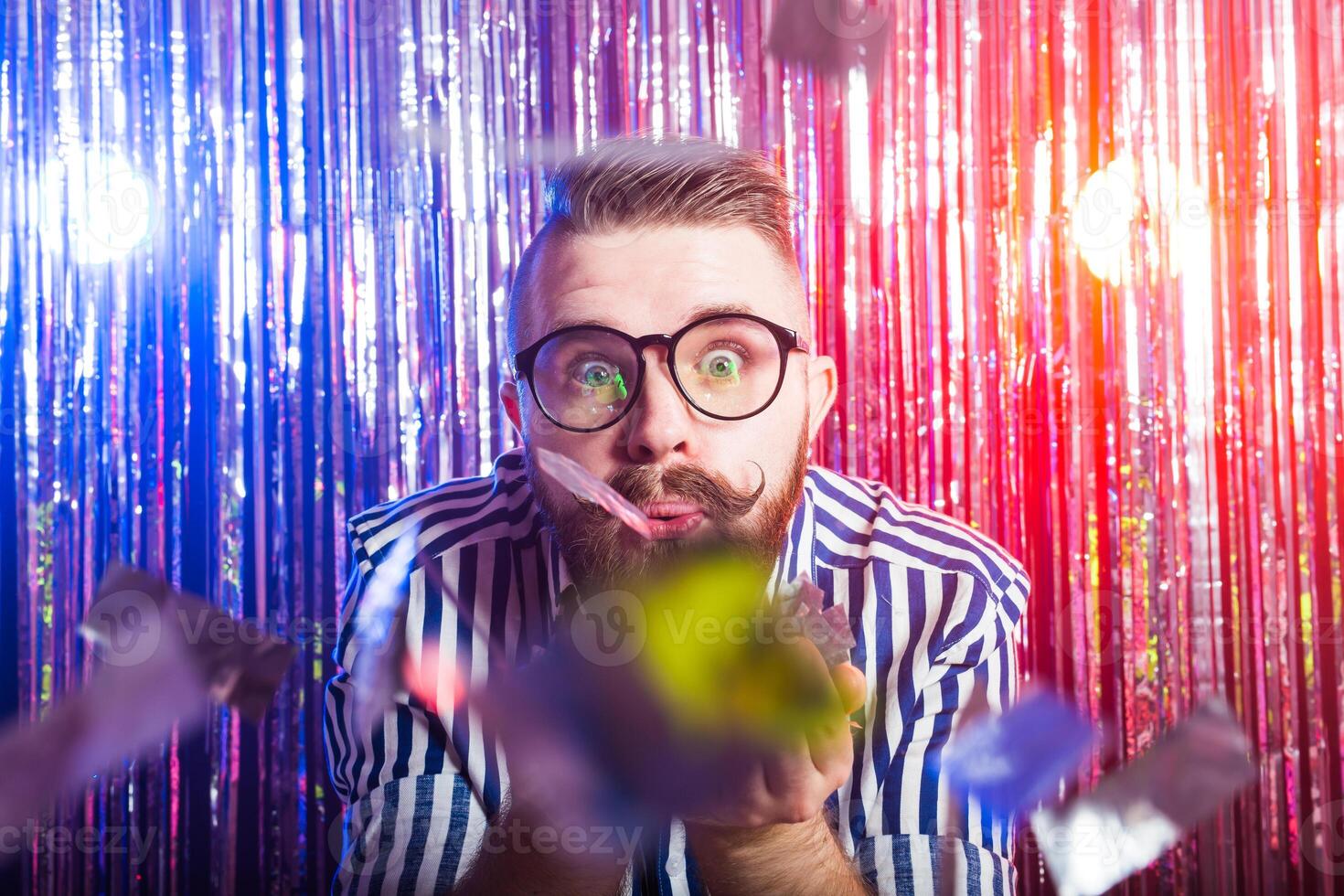 Party, carnival, holidays and fun concept - Fancy male blowing confetti against shiny background. photo