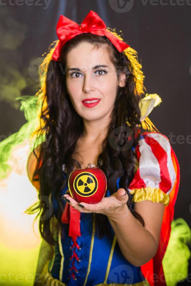 Pretty Female dressed as fairytale character holds Radioactive atomic nuclear ionizing radiation danger warning symbol on apple. Nuclear and radiation measurement concept. photo