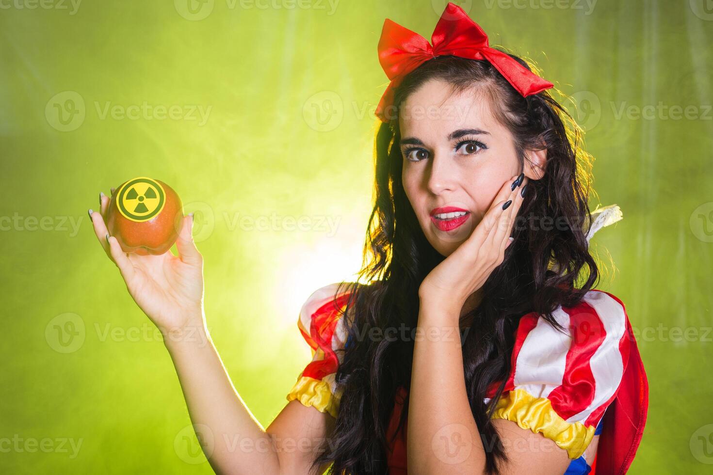 Portrait Surprised woman dressed as fairytale character holds Radioactive atomic nuclear ionizing radiation danger warning symbol on apple. Nuclear and radiation measurement concept. photo