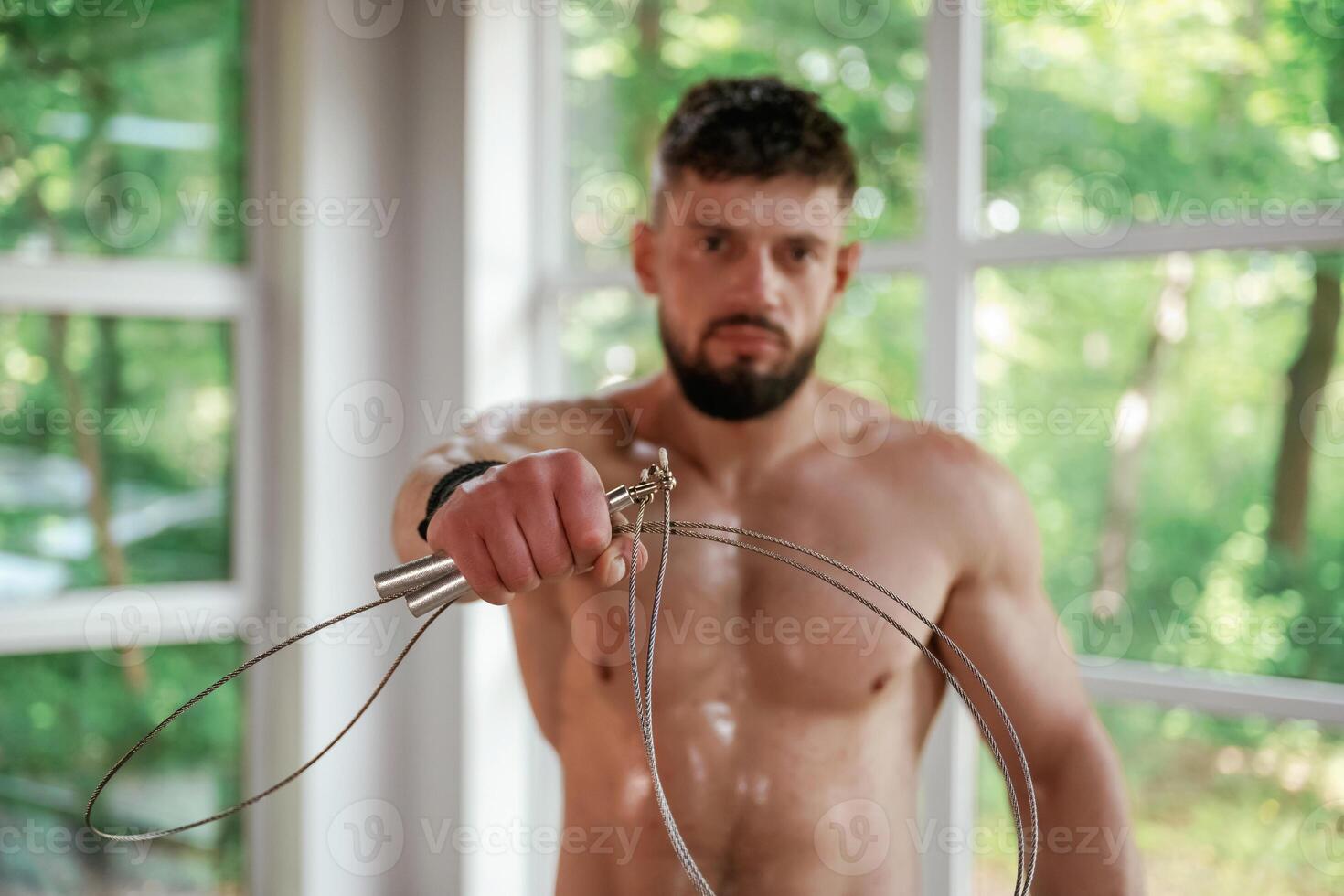 Holding jump rope. Strong muscular man is working out in the gym photo