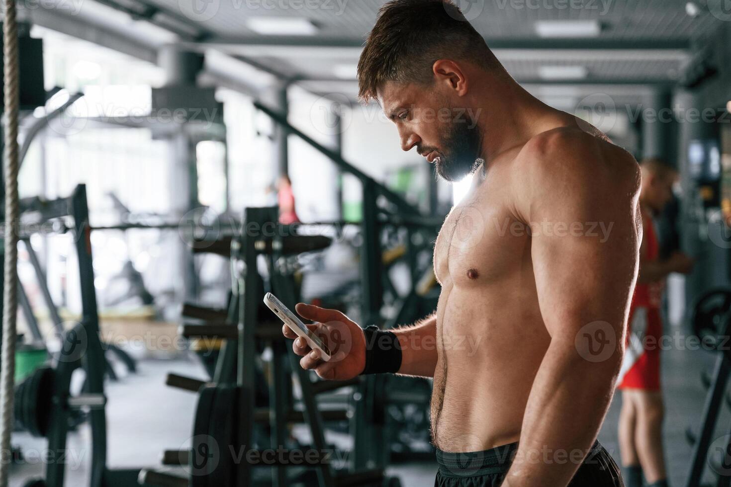 With smartphone, taking ,a break. Strong muscular man is working out in the gym photo