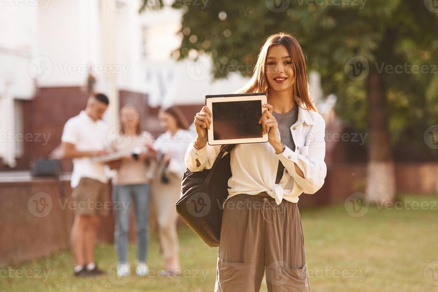 Woman is showing digital tablet, copy space. Group of students are outside together photo