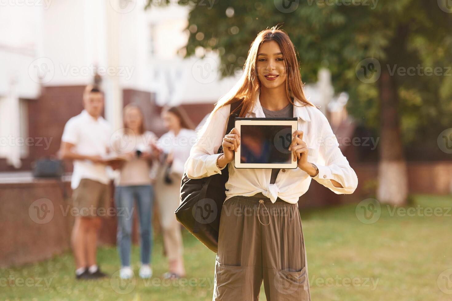 Woman, is showing digital tablet,,, copy space. Group of students are outside together photo