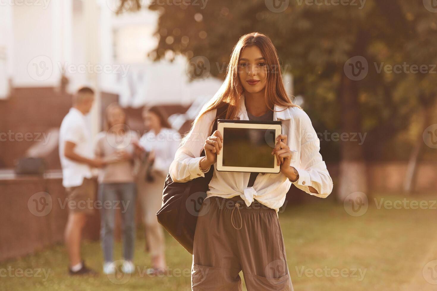 Woman is showing digital tablet, copy space. Group of students are outside t,,ogether photo