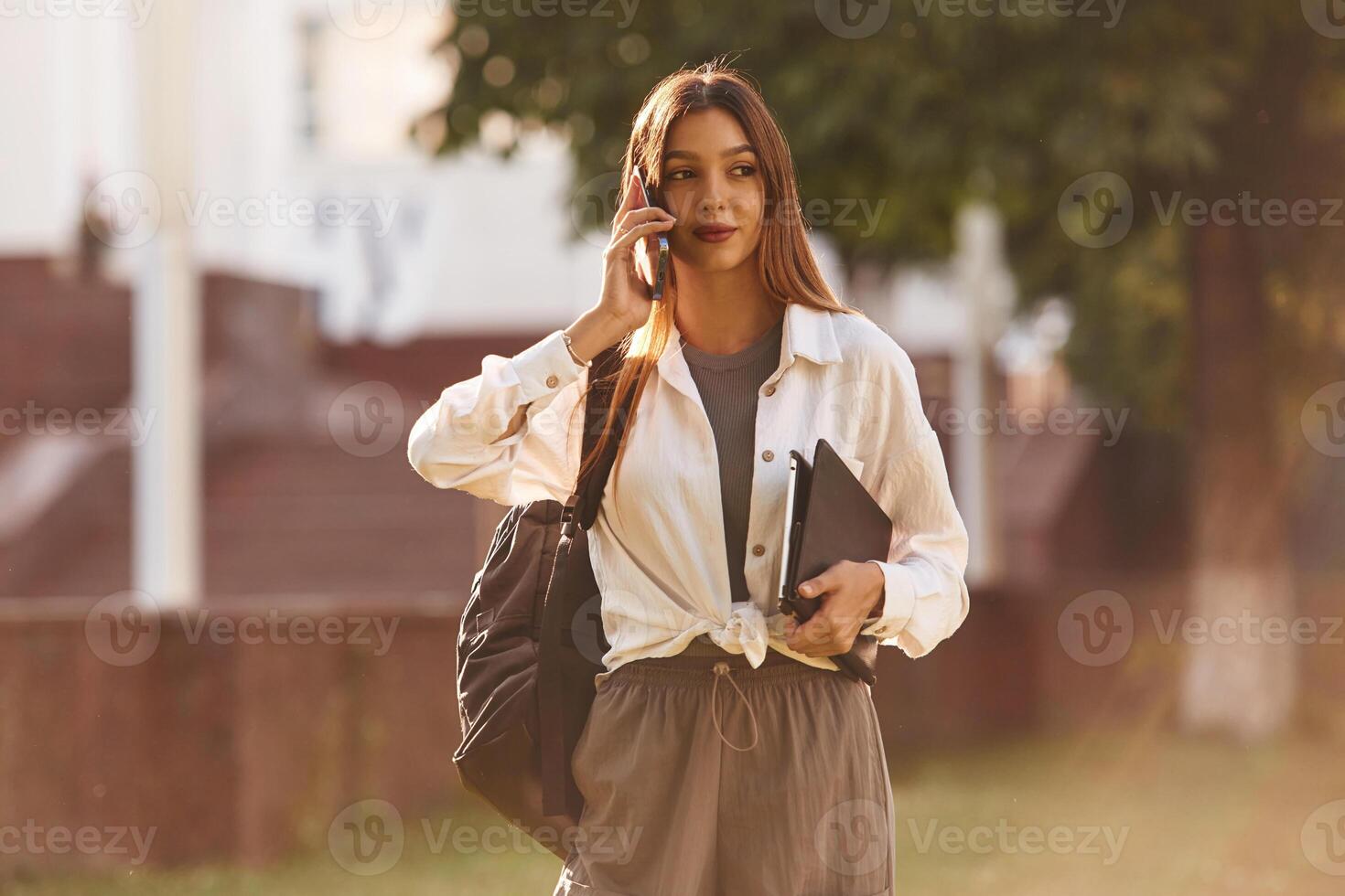 Talking by phone. Beautiful ,female,, student is outdoors near the university photo