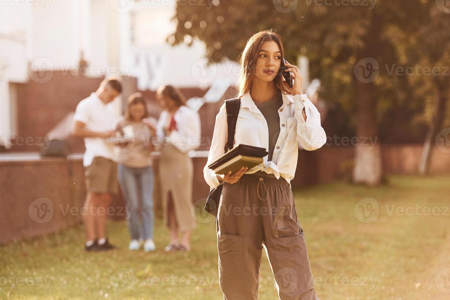 Beautiful woman is standing ,in ,,front of her friends. Group of students are outside photo