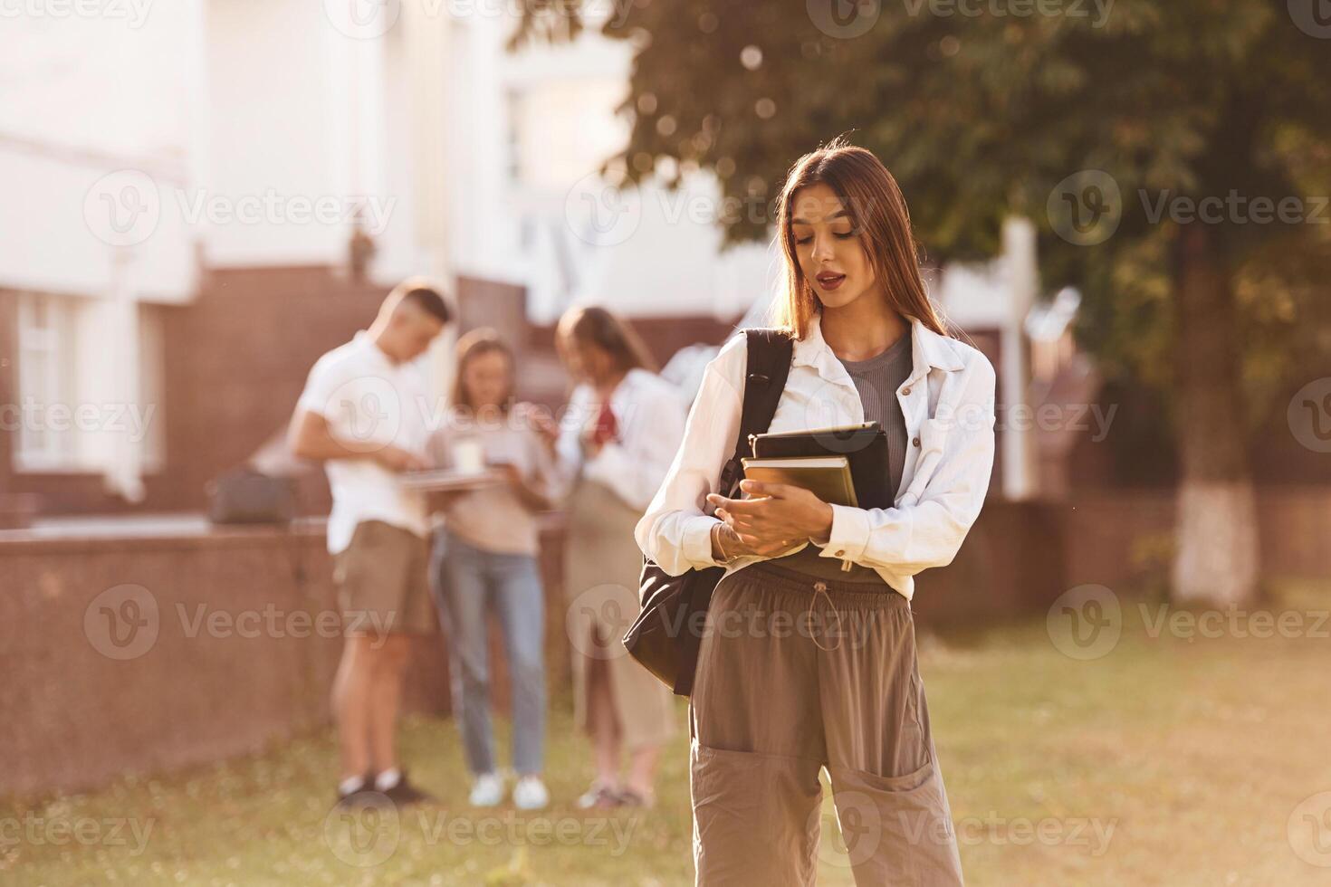 Beautiful woman is ,standing in front of her friends. Group of students are outside photo