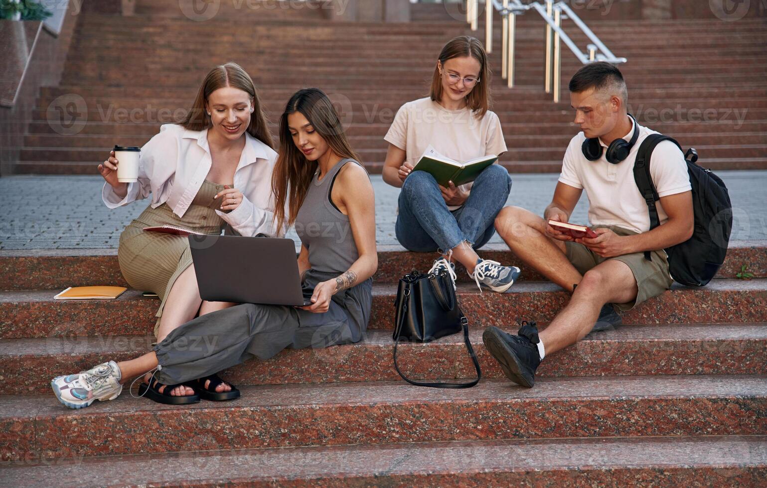 Relaxed,, on the stairs, with laptop. Group of students are outside together photo