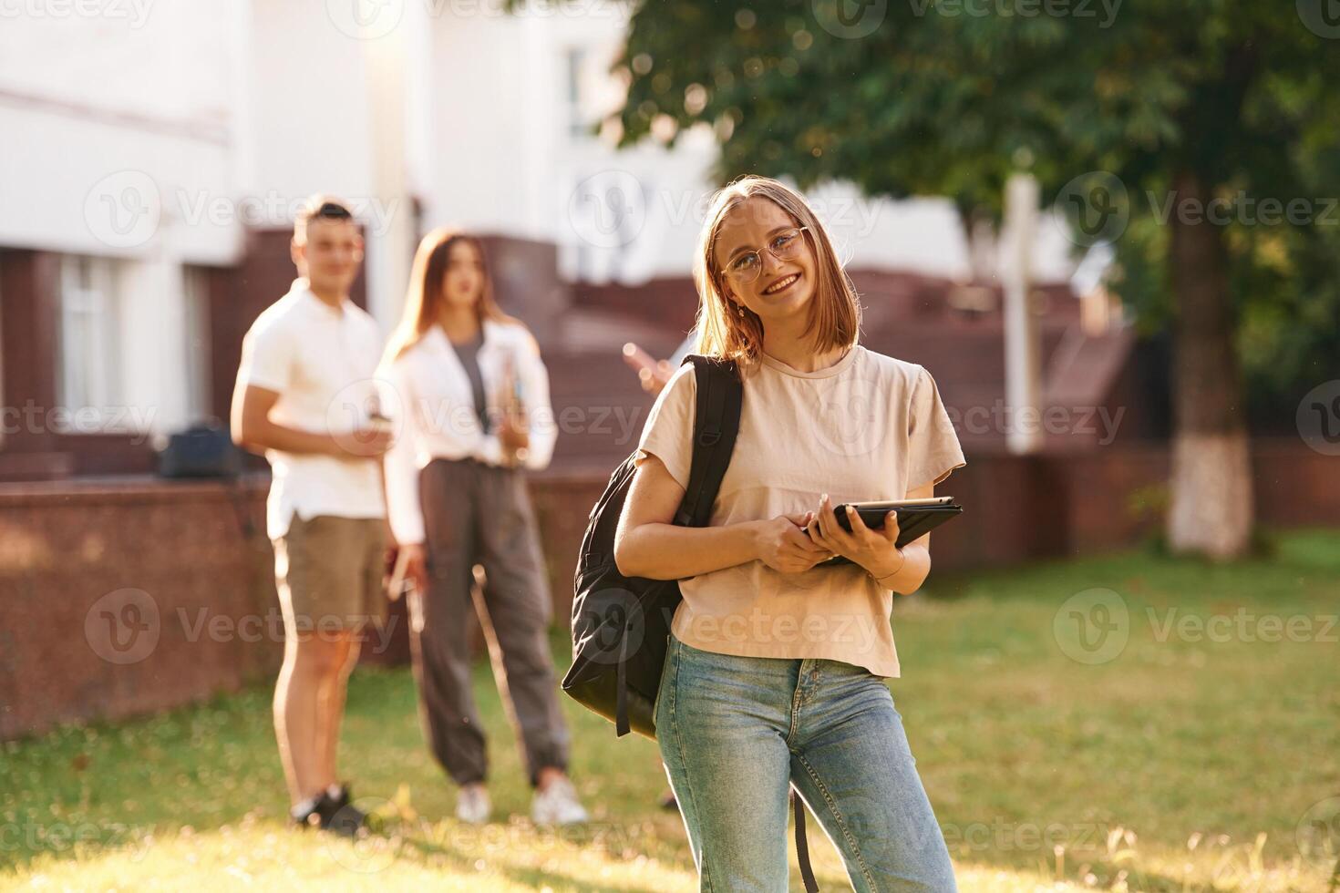 Girl is ,,with digital tablet. Group of students are outside together photo