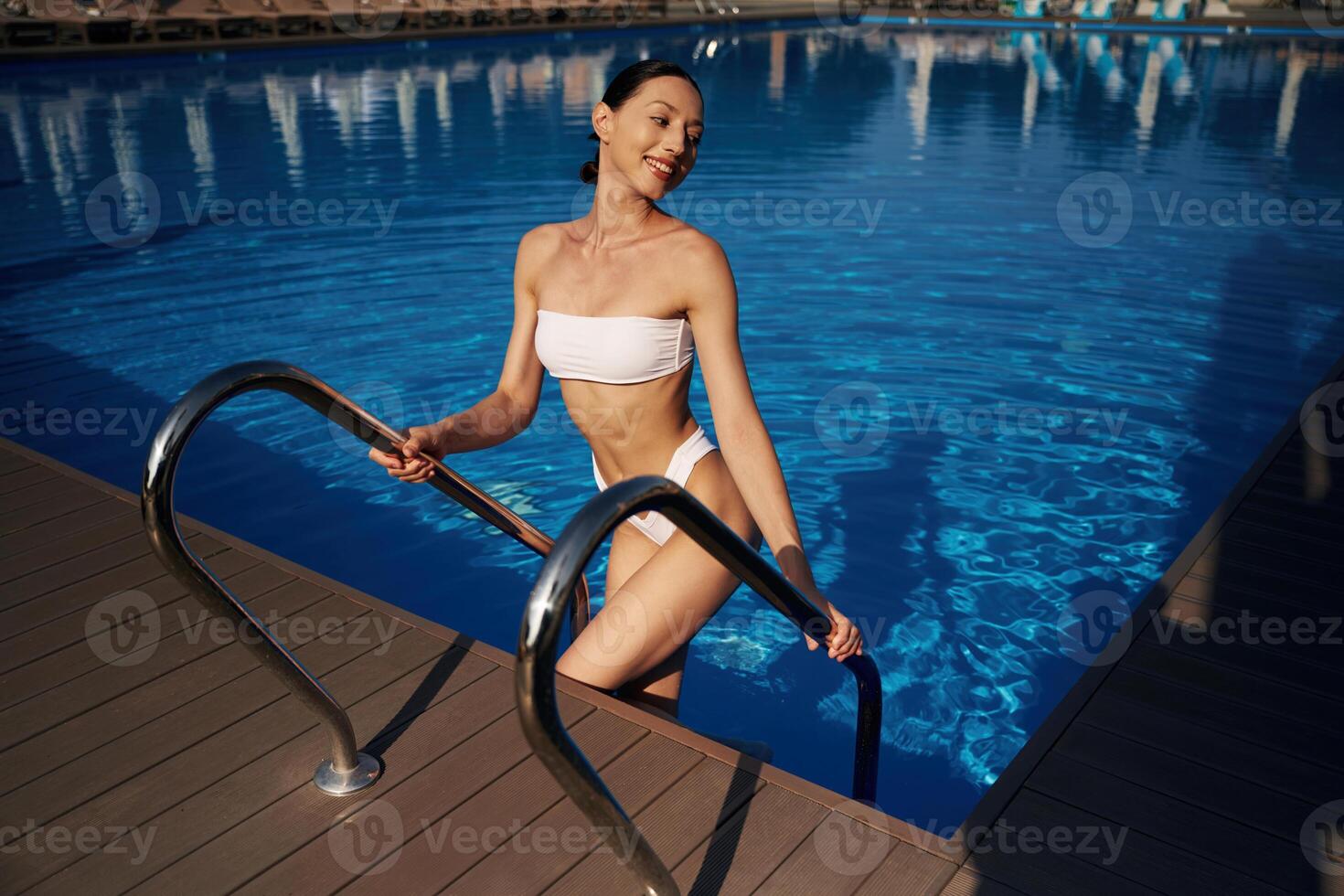 Going up ,out the water. Beautiful woman in bikini is resting by the pool photo
