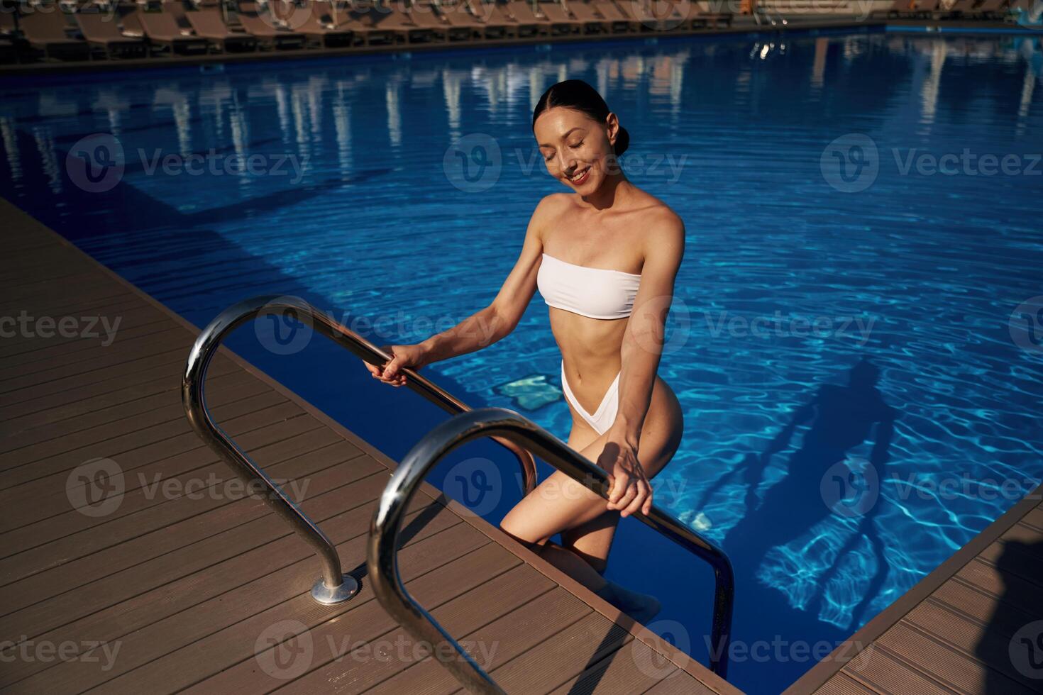 Going ,up, out the water. Beautiful woman in bikini is resting by the pool photo