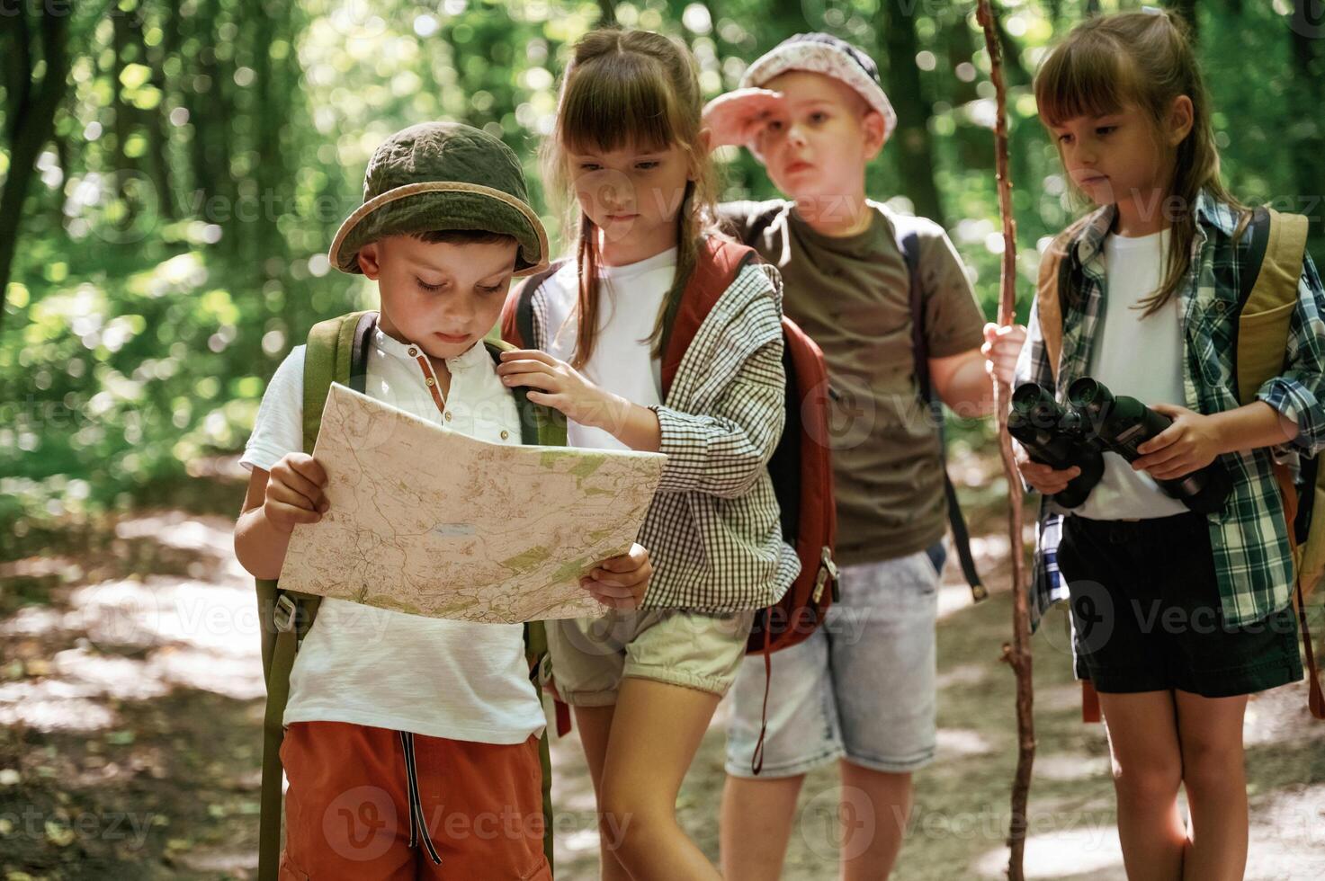Smart ,boy is, reading the map. Kids in forest at summer daytime together photo