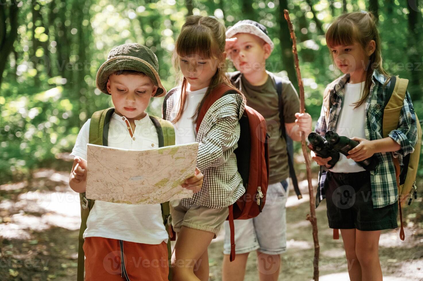 Smart ,boy is reading the map.. Kids in forest at summer daytime together photo