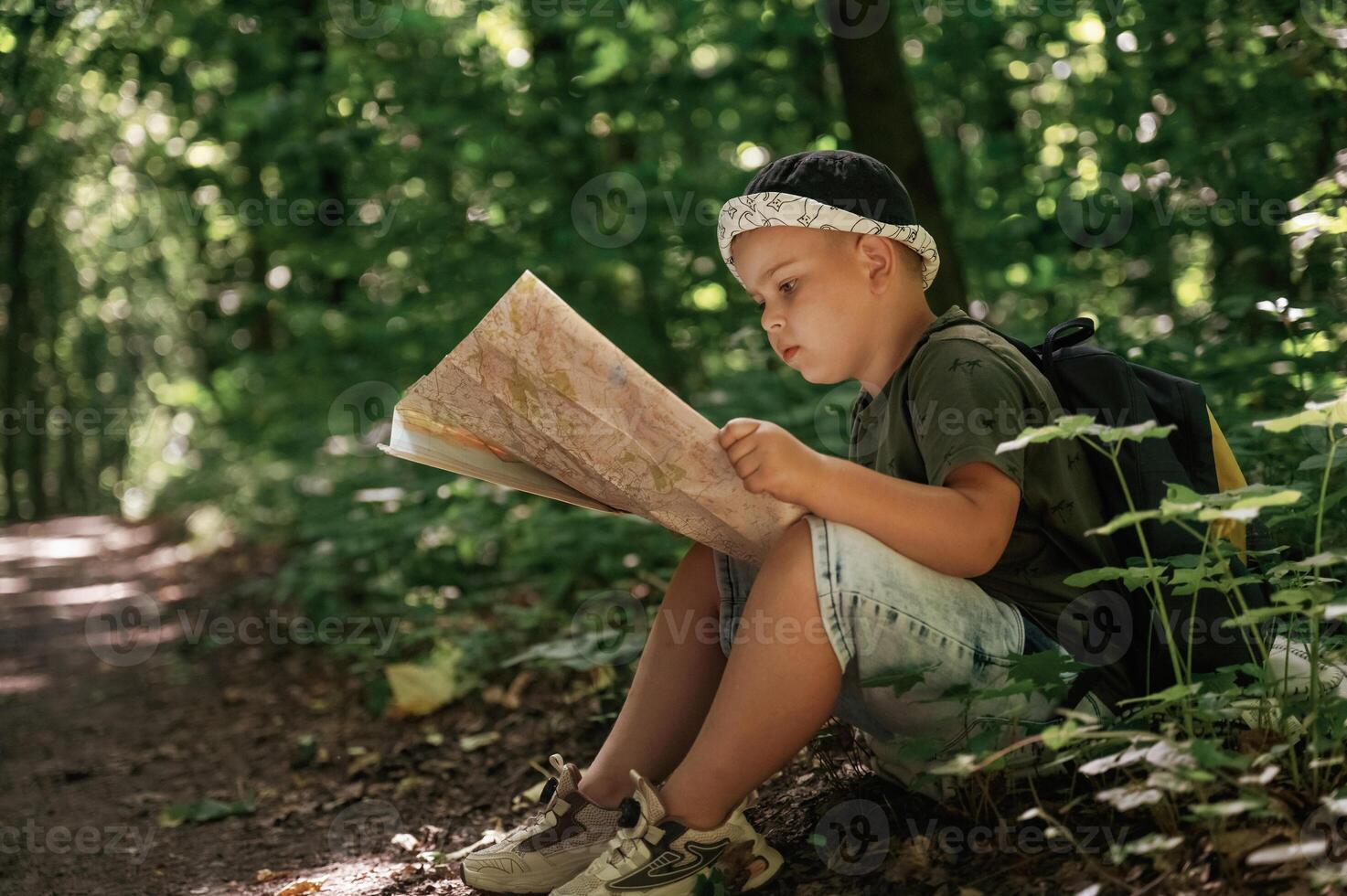 Little kid, tourist is sitting and reading the map in the forest photo