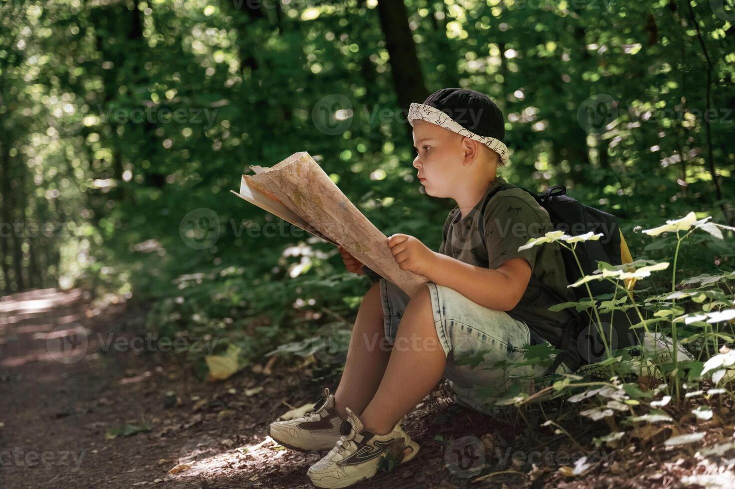 Little, kid tourist is sitting and reading the map in the forest photo