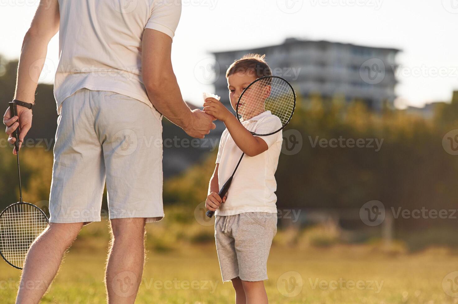 With badminton rackets. Father and little son are together on the summer field, photo