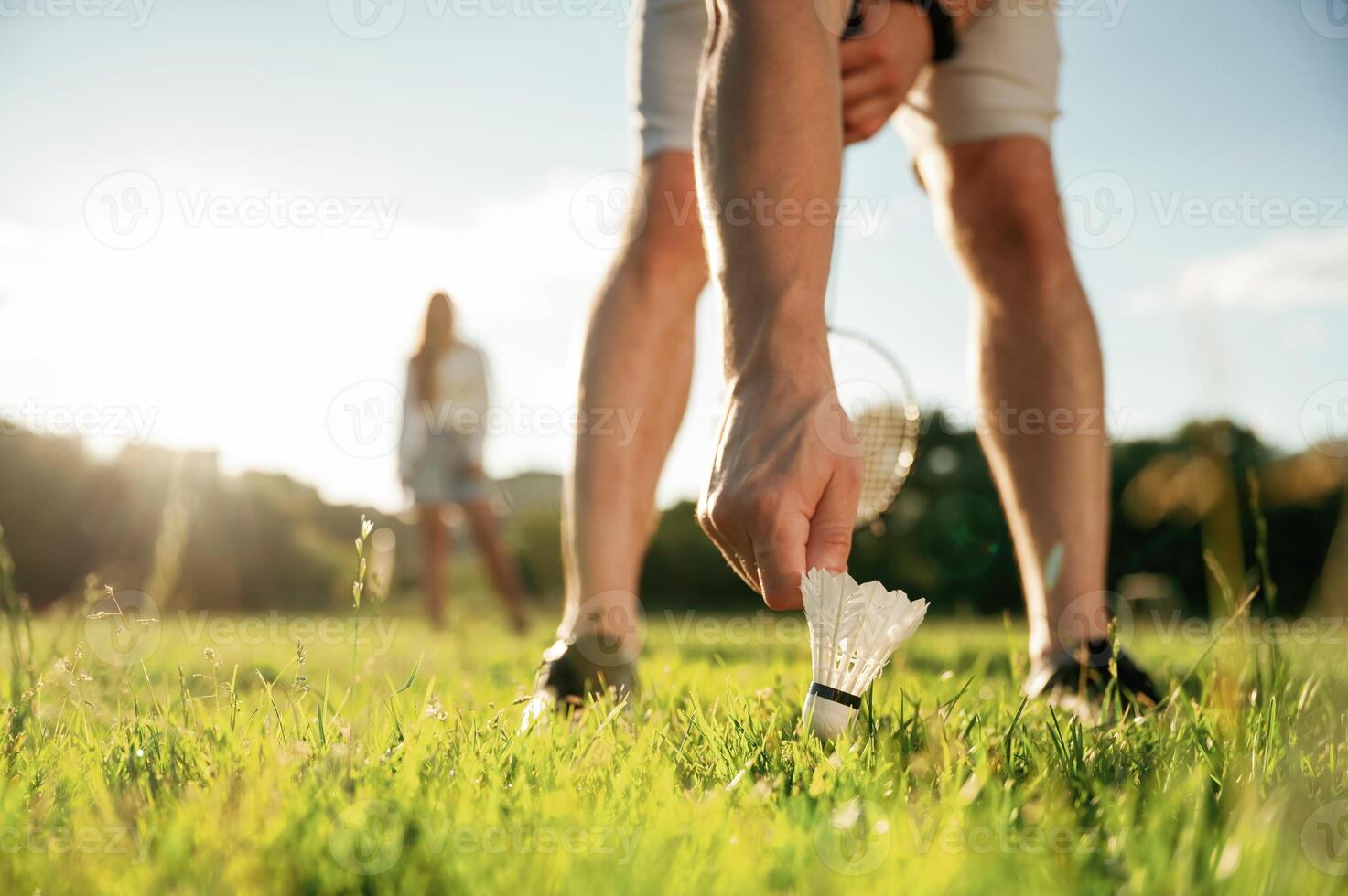 Guy is picking up the shuttlecock. Man with woman are playing badminton on ,the field photo
