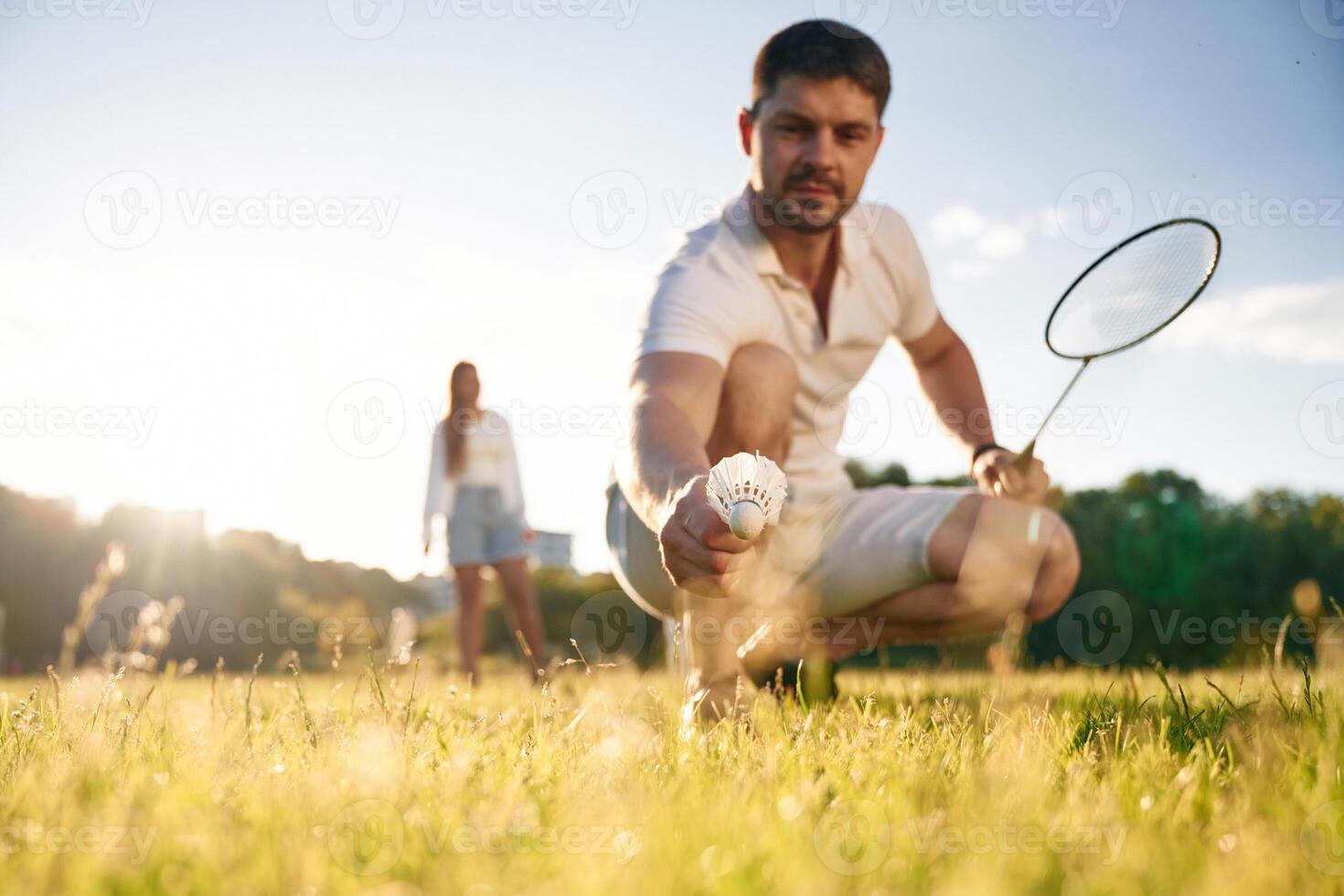 Fallen, shuttlecock, guy ,is, taking, it. Man with woman are playing badminton on the field photo