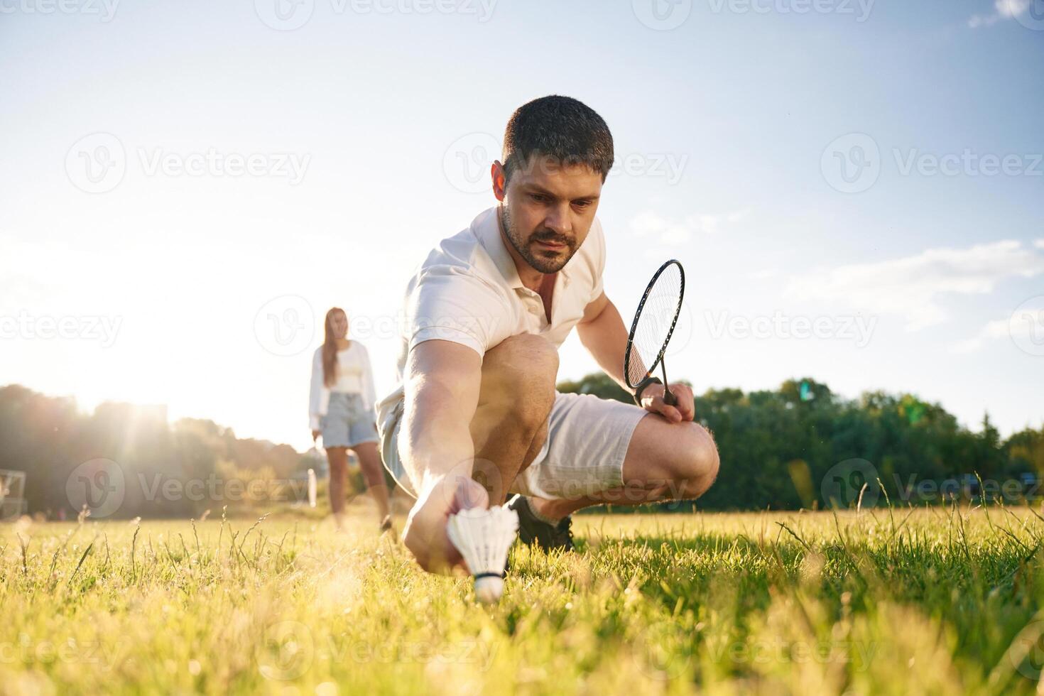 Fallen, shuttlecock, guy, is, taking it. Man with woman are playing badminton on the field photo