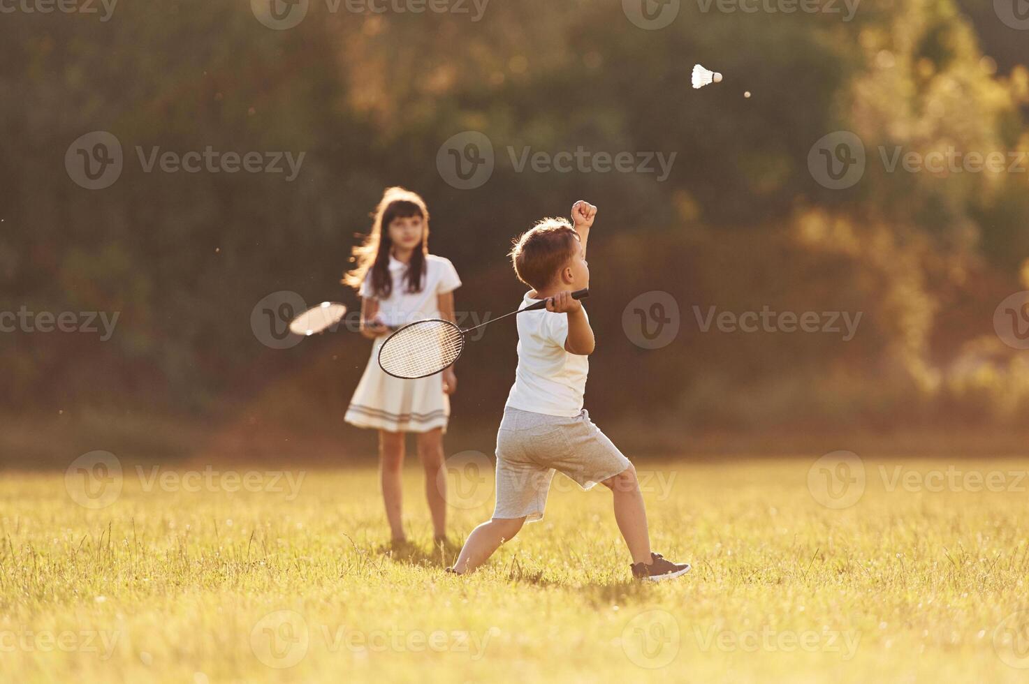 Rackets in hands, playing badminton.. Happy kids are on the summer field photo