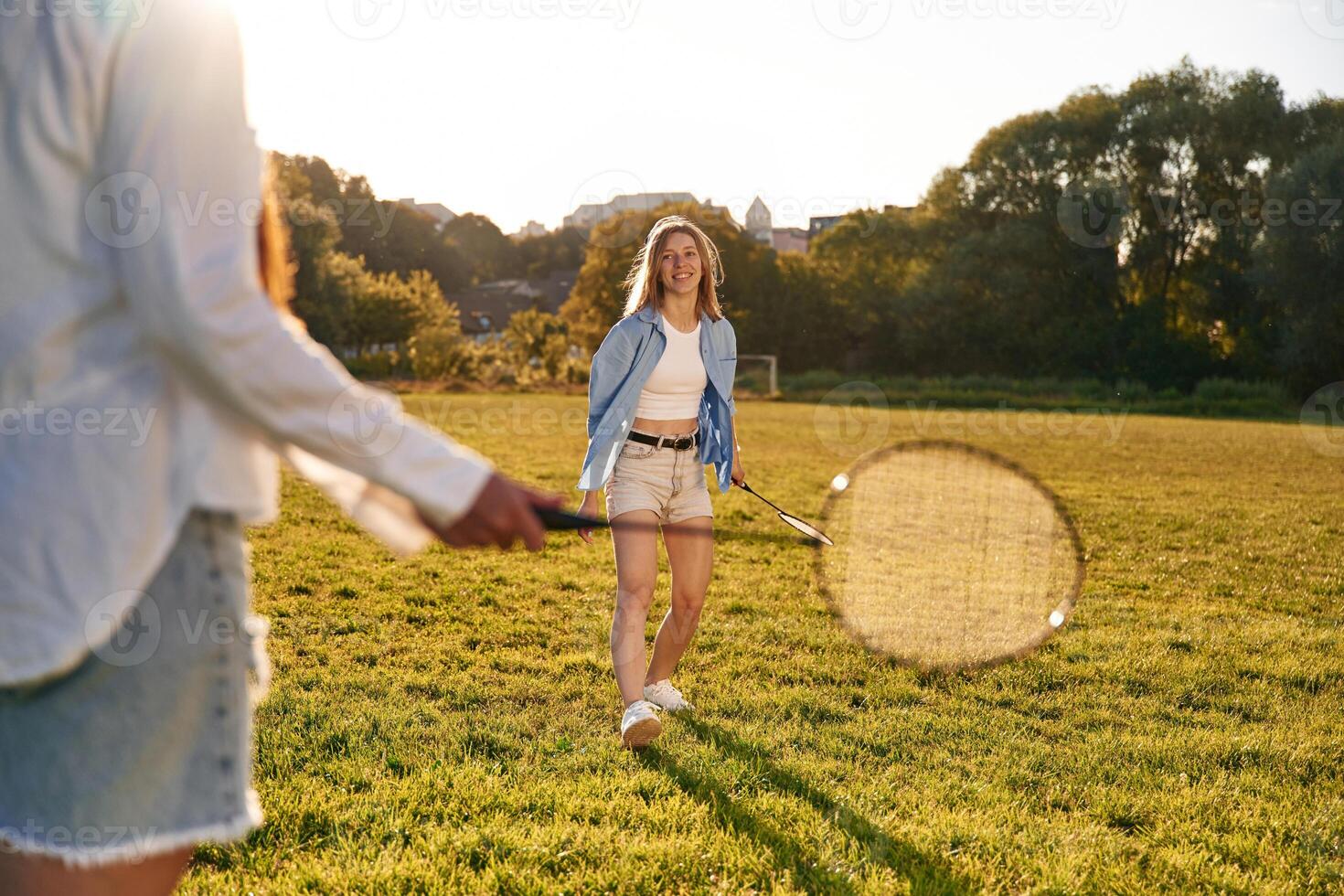 Two ,women are having,, fun, with badminton rackets, on the field photo